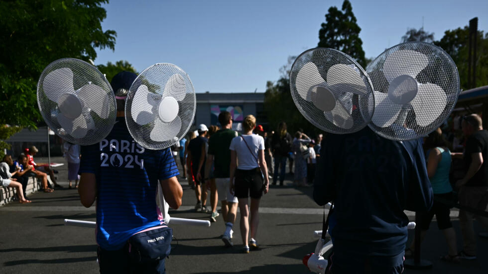 Des volontaires transportent des ventilateurs par une chaude journée d'été pendant les Jeux Olympiques de Paris 2024 devant l'Arena Paris Sud, le 29 juillet 2024